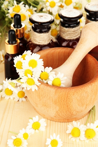 Essential oil and chamomile flowers in mortar on wooden table